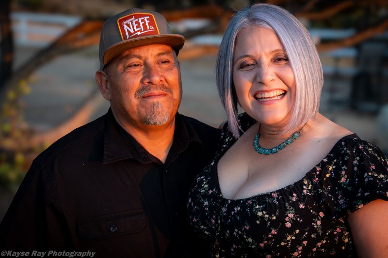 Smiling couple in golden-hour light, the man in a trucker cap and the woman with silver hair laughing warmly.