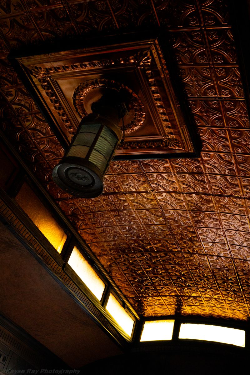 Ornate copper tin ceiling with a hanging lantern glowing in warm amber light