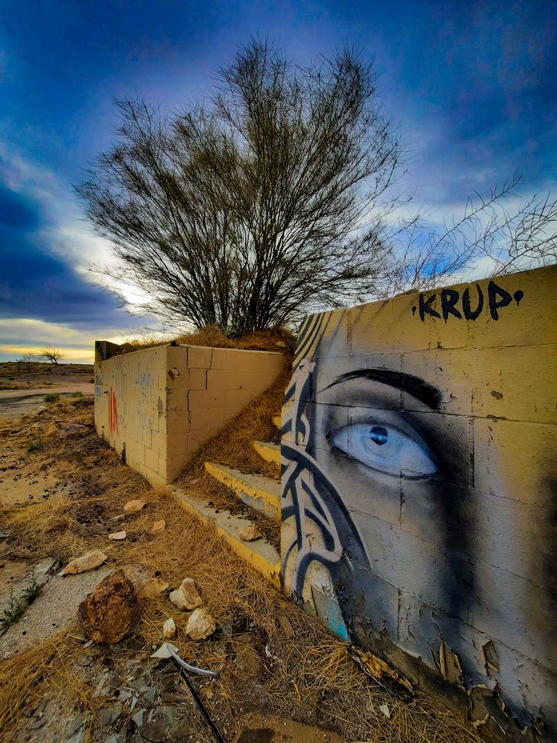 Graffiti of a piercing eye on an abandoned desert ruin under a stormy twilight sky