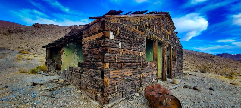 Abandoned cabin built from railroad ties with a rusted barrel out front in a remote desert valley